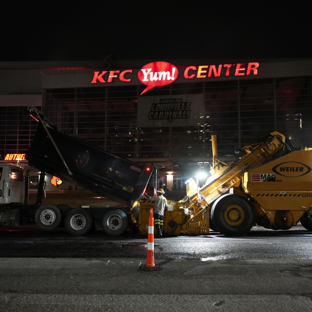 Nighttime view of the KFC Yum Center with active construction equipment in the foreground and workers nearby.