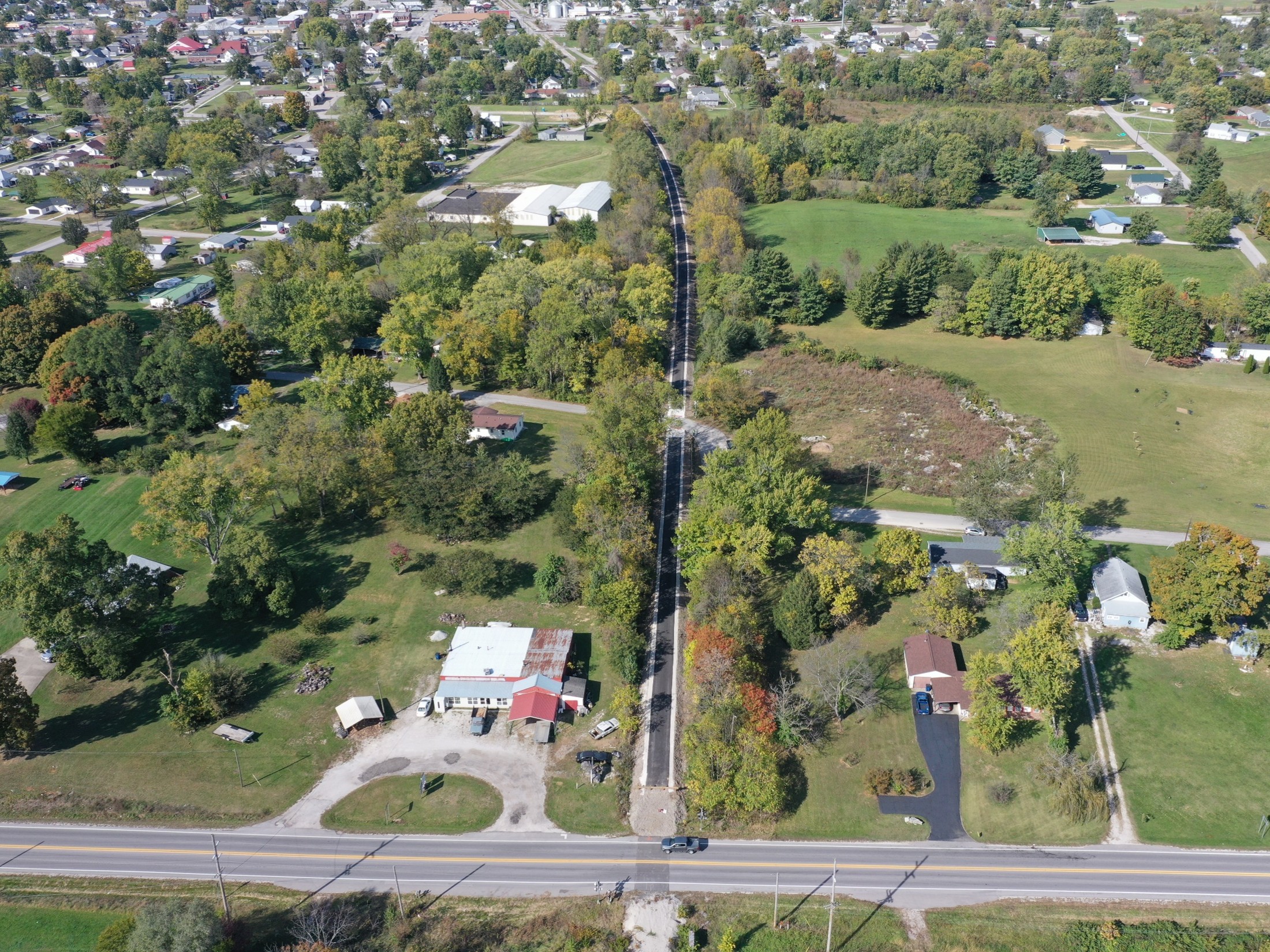 Aerial view of a small town with a tree-lined road running through residential neighborhoods and surrounding green fields.