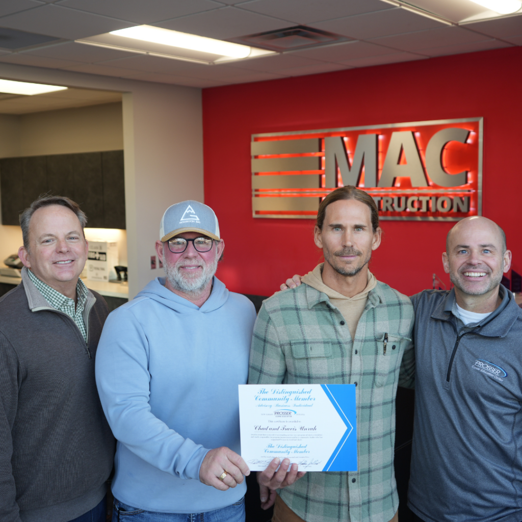Four men stand together in a MAC Construction office lobby, smiling; one man holds a blue-and-white certificate.