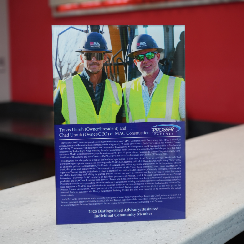 Two men in yellow safety vests and hard hats pose for a MAC Construction brochure on a table.