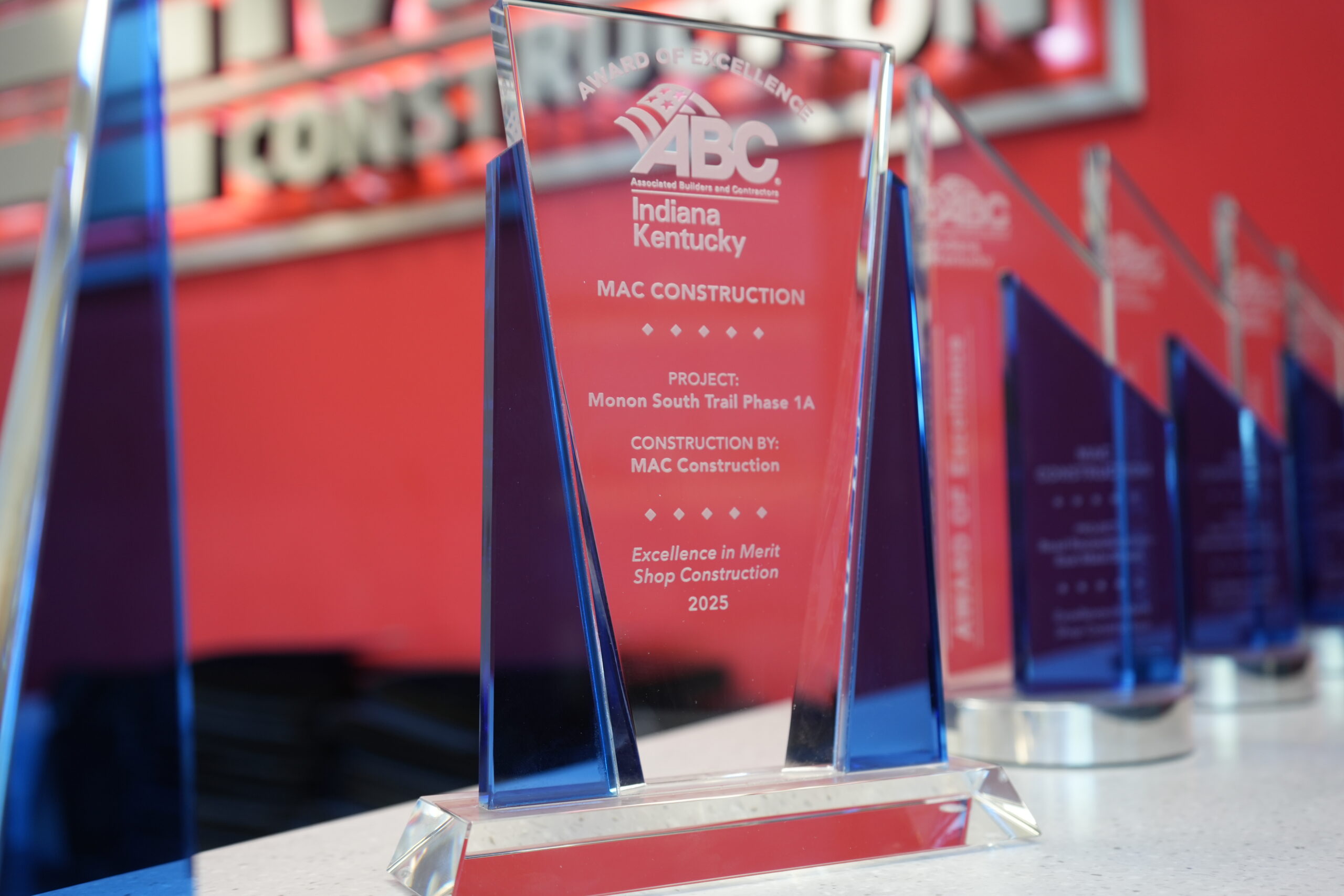Crystal trophy with a red panel reading ABC Indiana Kentucky MAC Construction and Excellence in Merit Shop Construction 2025 on a display shelf.
