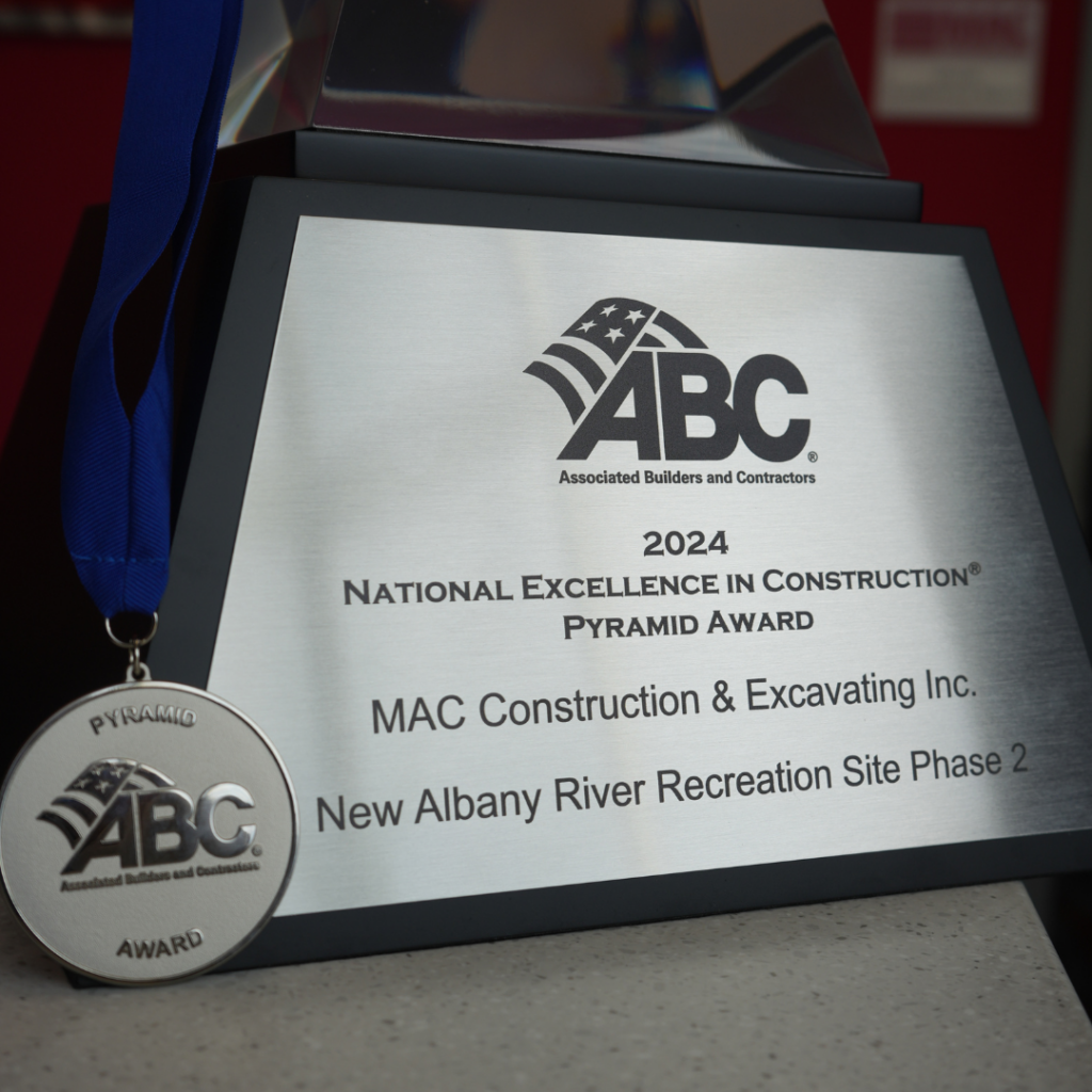Silver plaque reads '2024 National Excellence in Construction Pyramid Award' for MAC Construction & Excavating Inc., New Albany River Recreation Site Phase 2, with a round ABC medal on a blue ribbon beside it.