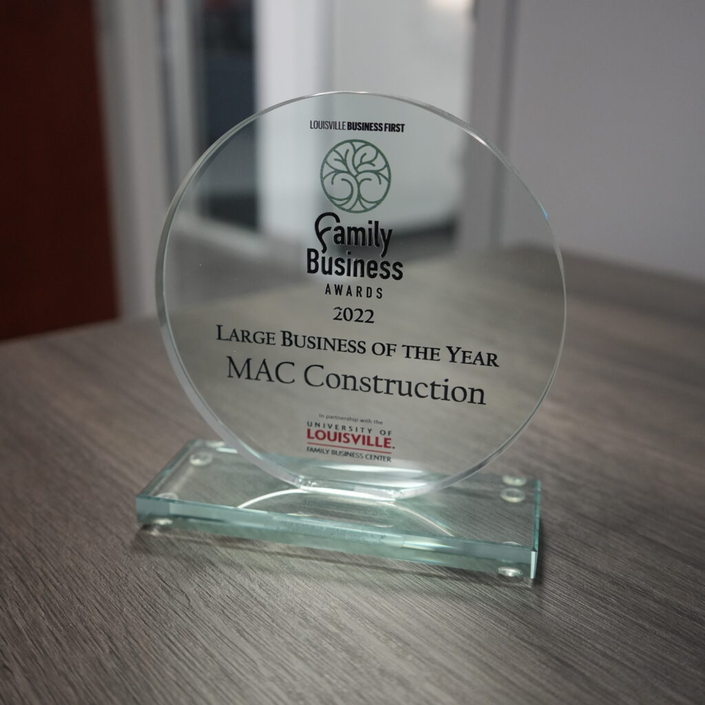 Circular glass trophy on a glass base, inscribed with 'Family Business Awards 2022' for MAC Construction, on a wooden table