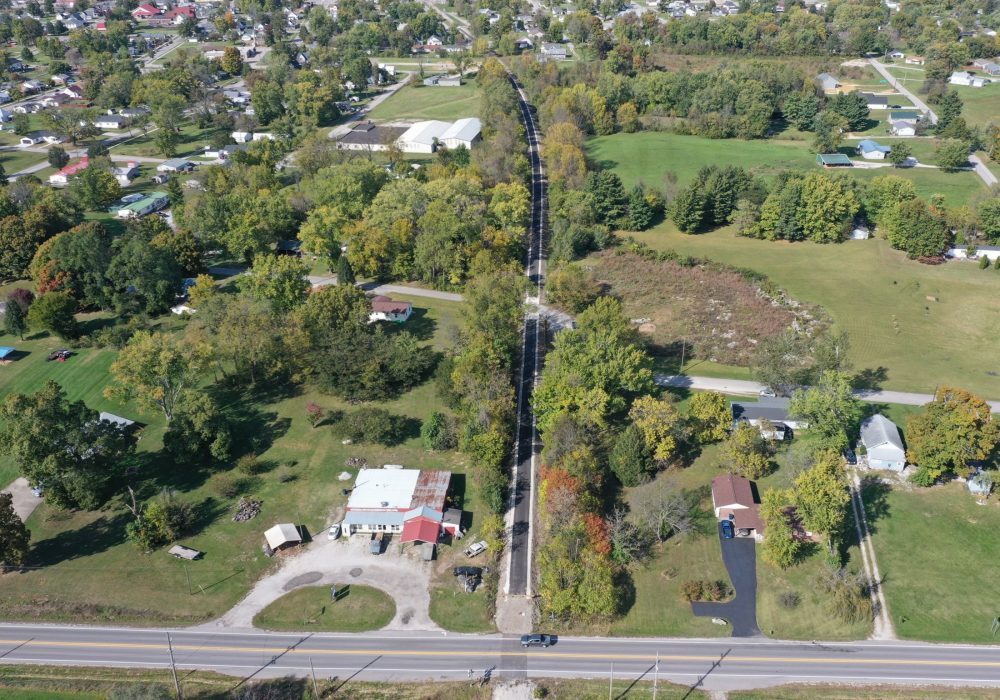 Aerial view of a small town with a tree-lined road running through residential neighborhoods and surrounding green fields.
